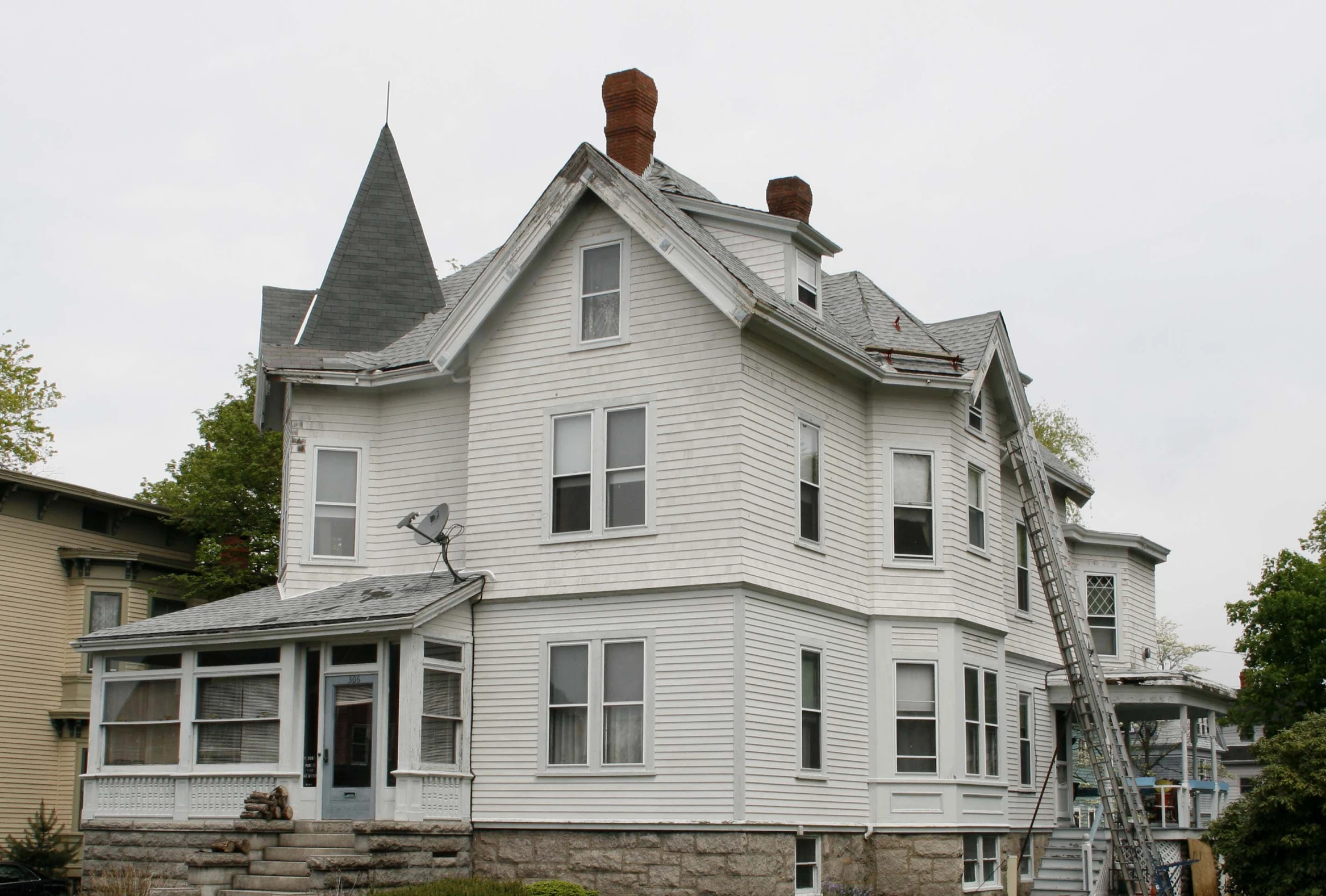 two white houses side by side one has a red fire hydrant and the other is a tall house with an ornate tower and black roof