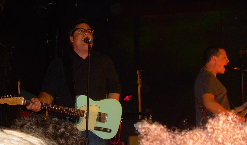 a man singing into a microphone next to another guy playing the guitar