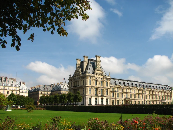 an old style building on the grass near many flowers