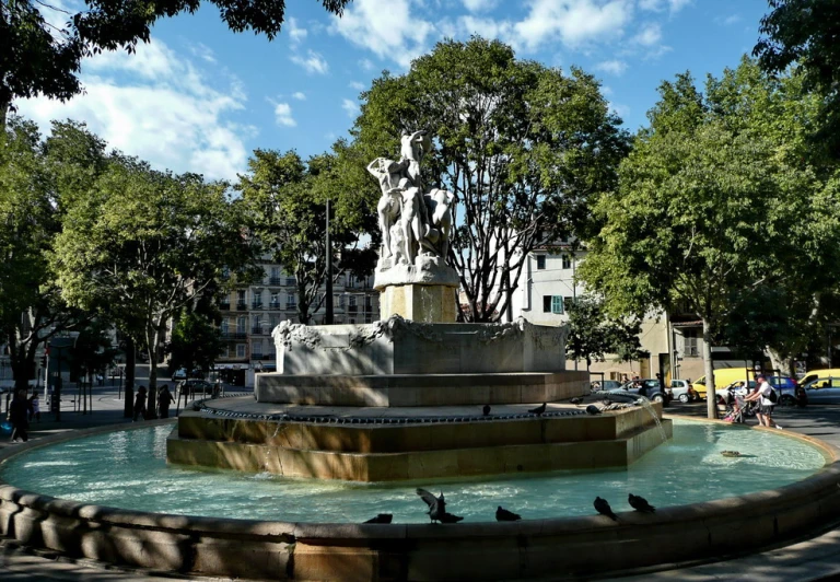 some pigeons are flying around the fountain of an urban park