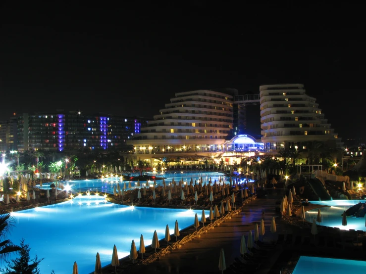 an illuminated swimming pool at night, with buildings in the background