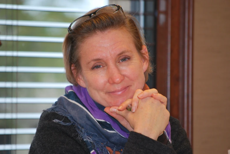 a woman poses with her hands crossed near her chin