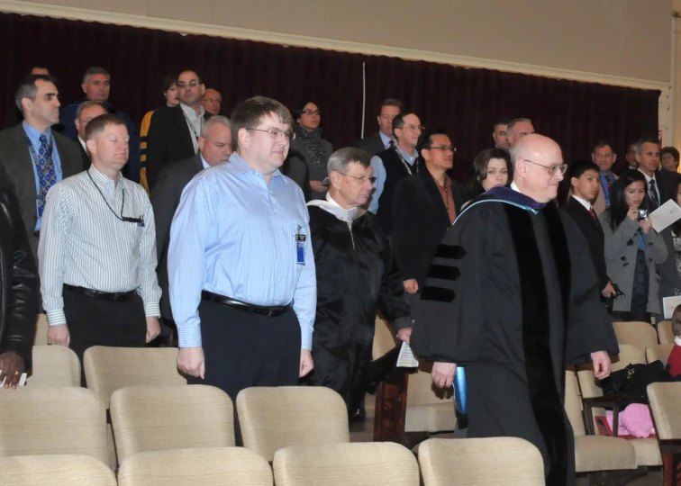 several men in graduation robes walking towards a crowd