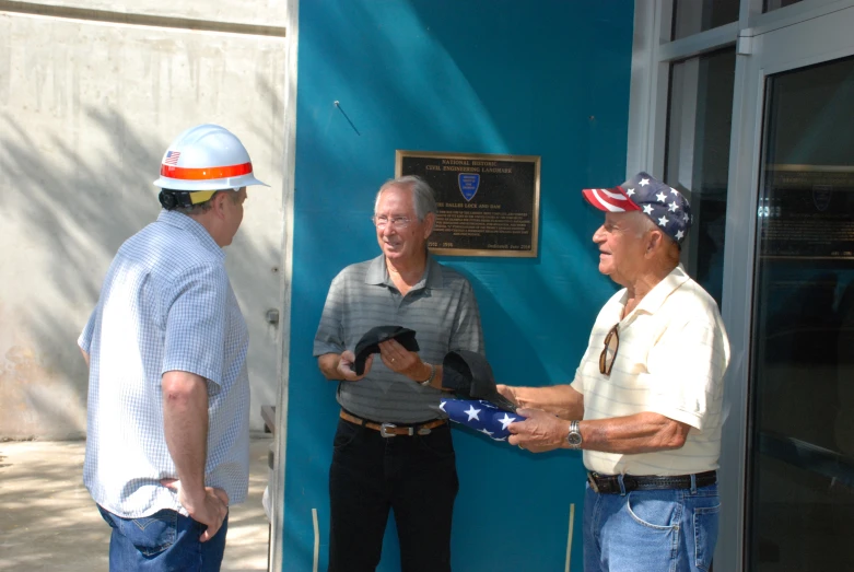 three men with hats, talking and one holding an american flag