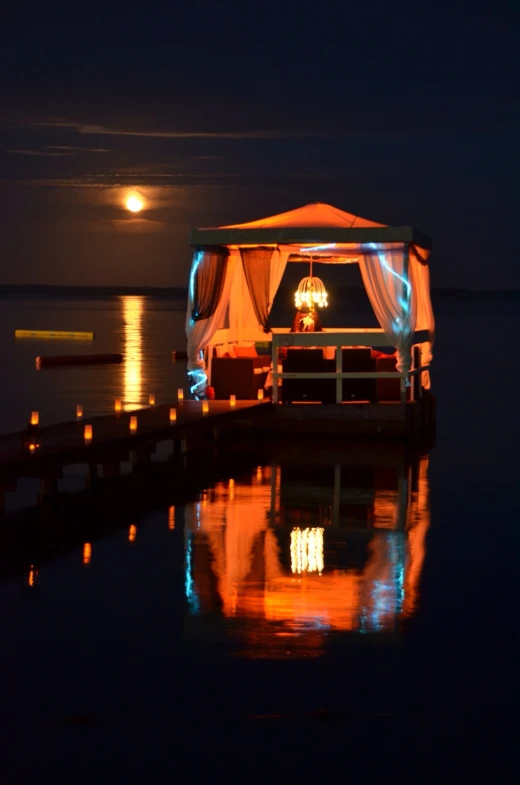 a tent on the water with a full moon behind it