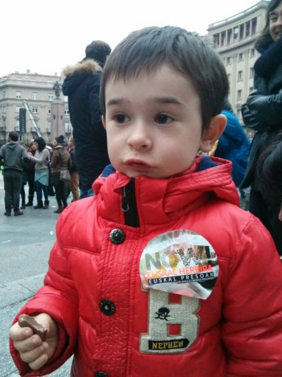 a close up of a child in a red jacket on a city street