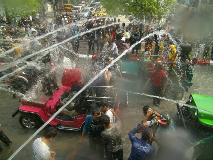 a group of people gathered together on the street near a splashing water cannon