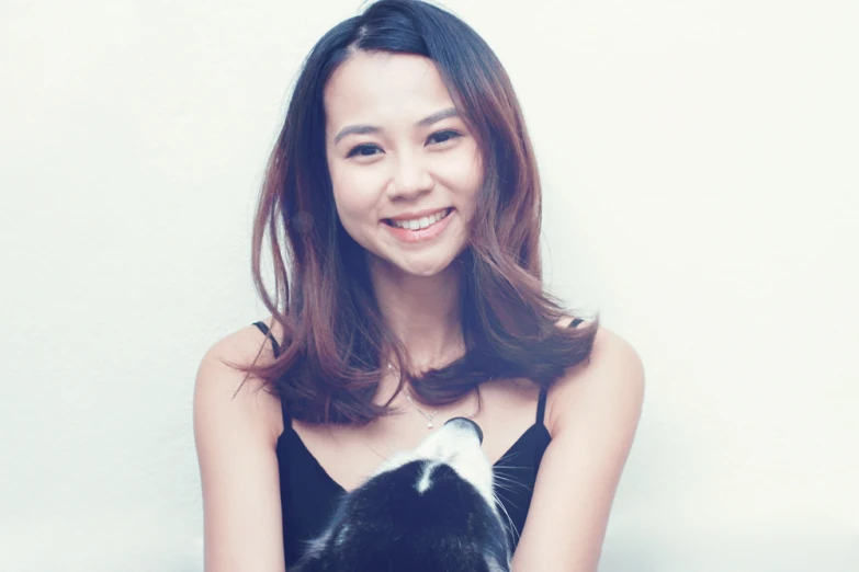 a woman smiles as she holds a black and white cat