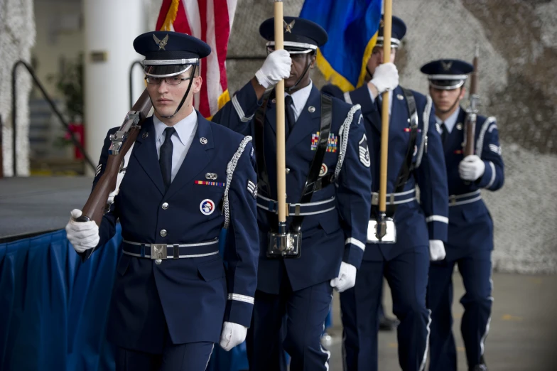 military men in blue uniforms stand at attention with flags