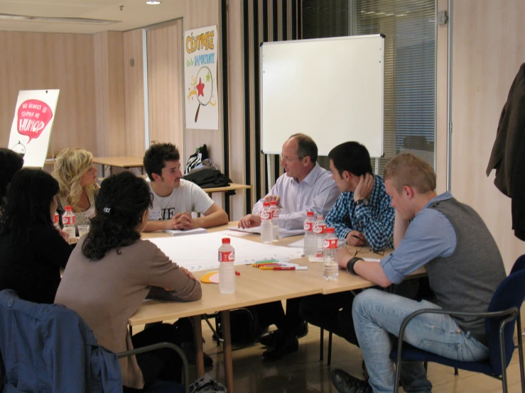 six men and women are sitting around a table with food