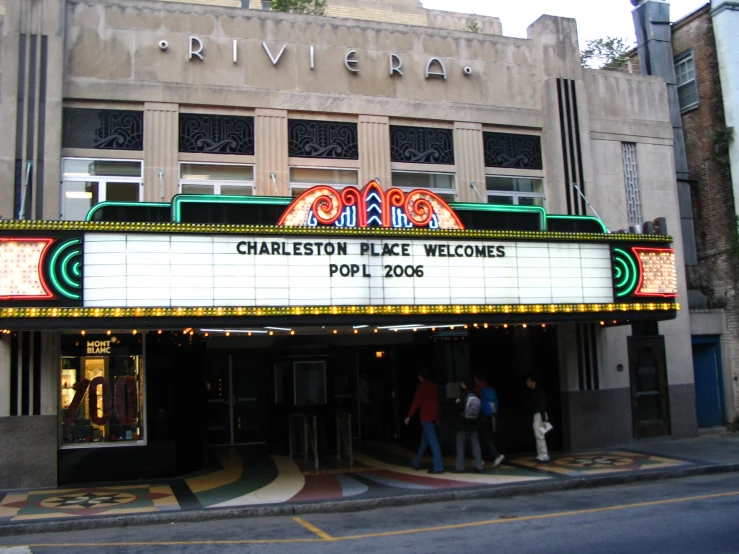 people walk through the entrance to a theater on a corner street