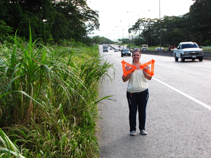 a person holding up an orange kite while standing on the side of the road