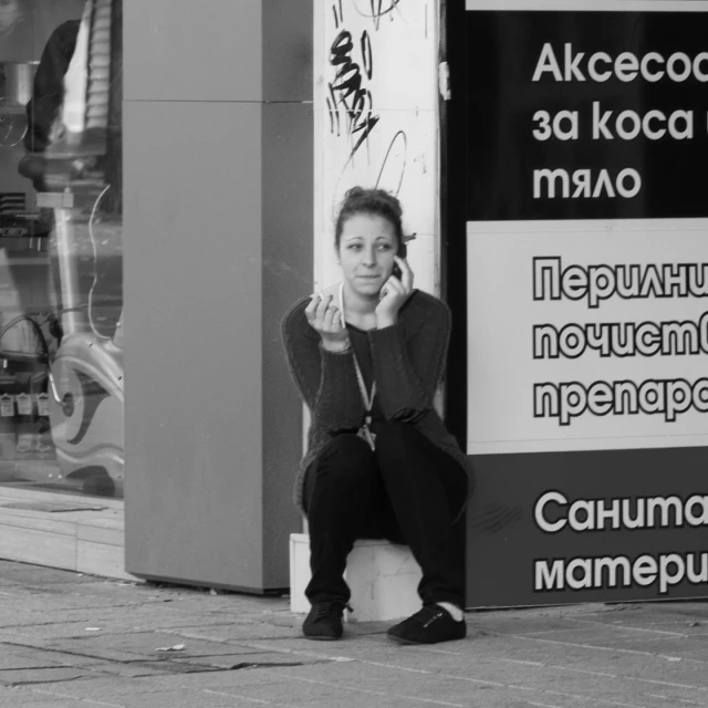 a black and white po of a woman sitting on the corner of a street with her hands in her ears