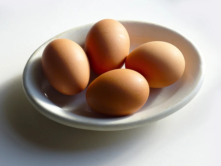 three brown eggs are in a white bowl