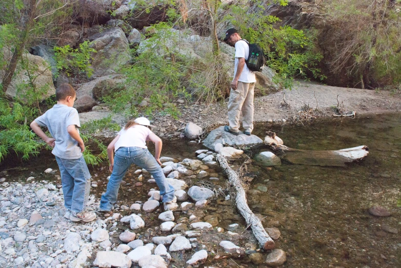 two boys are walking across a small river