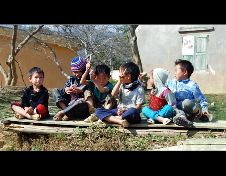 five boys are sitting in the grass on some wooden planks