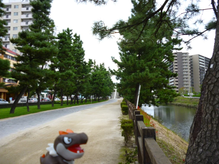 a toy horse sits on a bike in the foreground of a park area, surrounded by trees and tall buildings