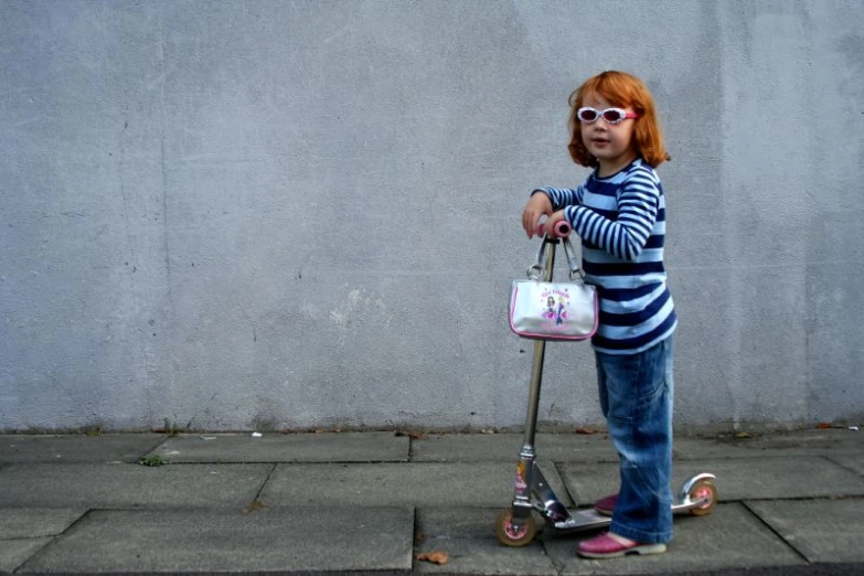 little girl standing on scooter holding up a bag