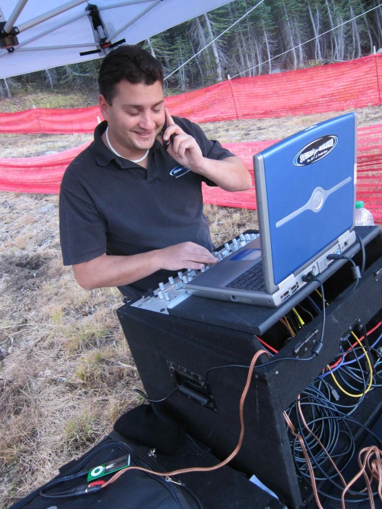 a man on his cell phone works on the laptop