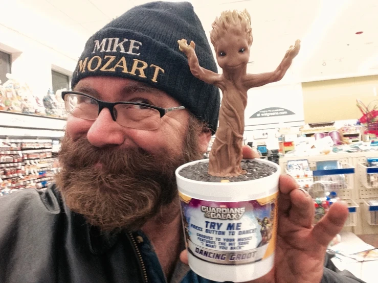 a man holding up a cup of ice cream with a small alien statue in the background