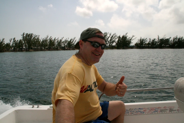 a man in a yellow shirt on a boat giving thumbs up