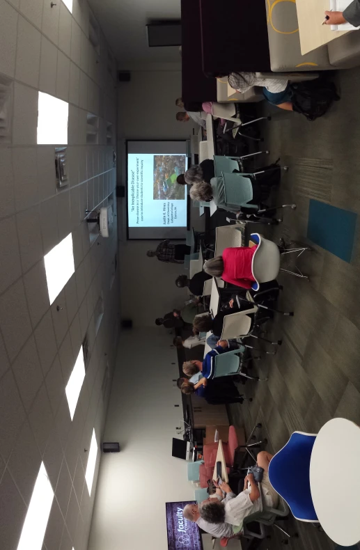 a group of people sit in chairs watching a presentation