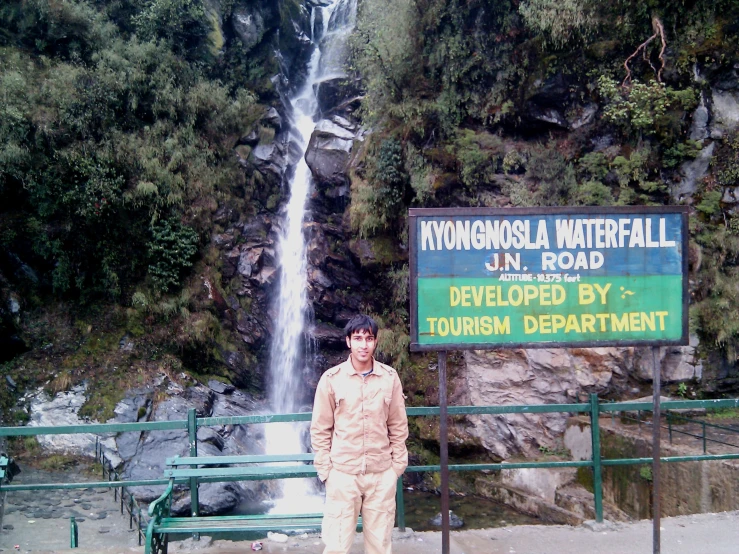 man standing in front of a sign next to a waterfall
