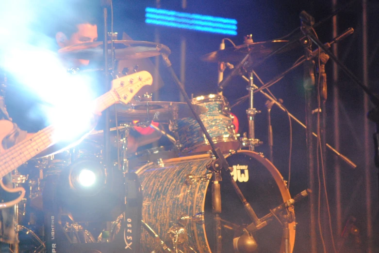 a guitar player sits at the front of a drum set