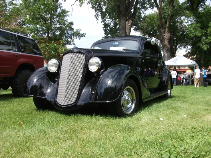 an antique car sits parked in the grass with people