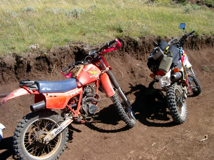 two motorcycles parked side by side on the dirt