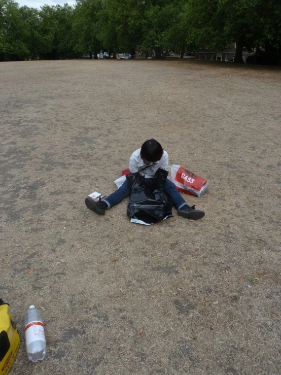 a person is sitting on the ground with a backpack, a bag, and two drinks