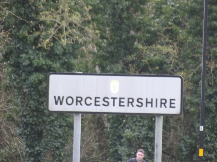 a man in black standing underneath an sign near some trees