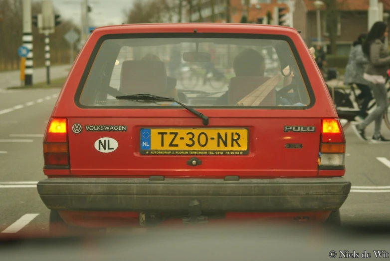 a red car with a yellow license plate driving down a road