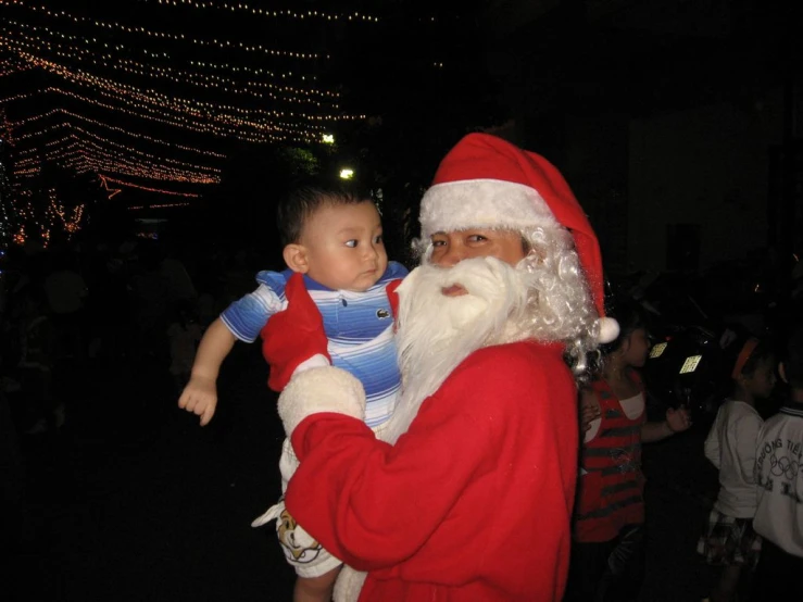 a person holding a little boy near a man in santa claus