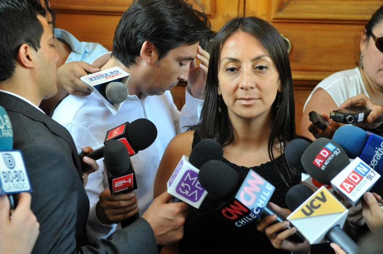 an asian woman in black speaks to reporters while standing around