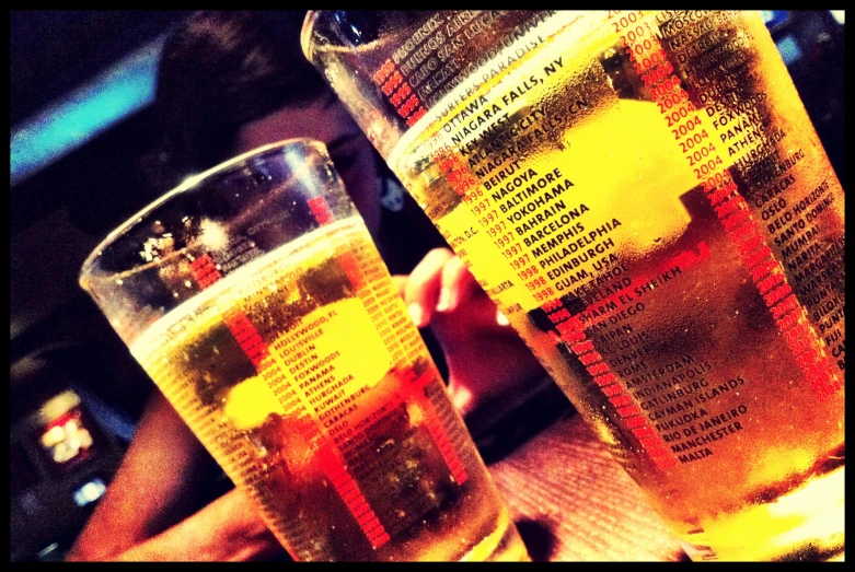 two beer glasses full of liquid being held by someone's hands