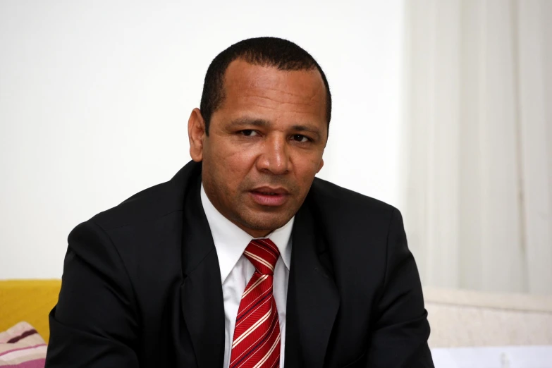 a man wearing a red tie and a suit in front of white wall