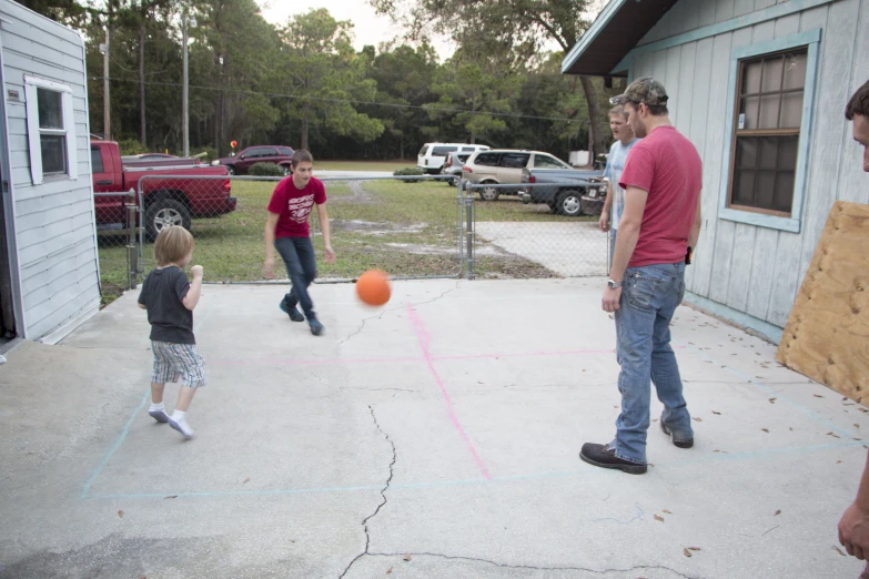 three men and two young children playing with an orange ball