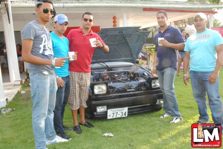 three men standing next to an under the hood car