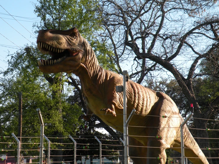 a dinosaur statue is standing by the fence