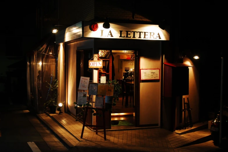 a dark street at night, with lights turned on and signage advertising different wines