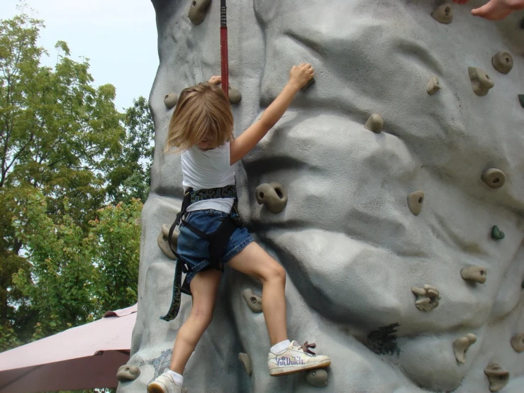 the little girl is climbing on the rock wall