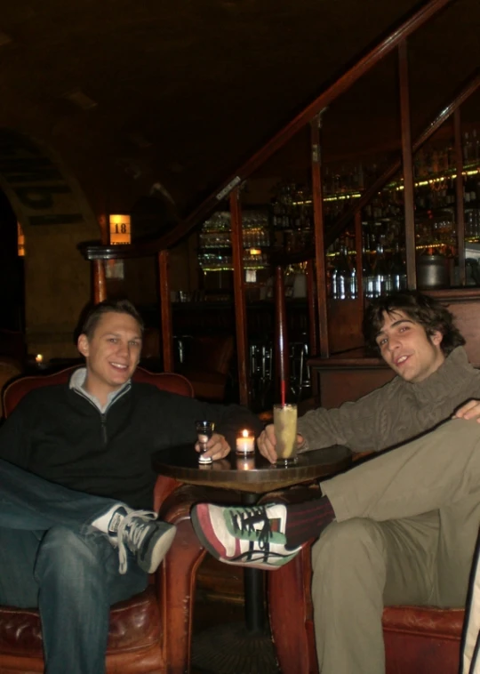 two men sit and smile while eating food at a table