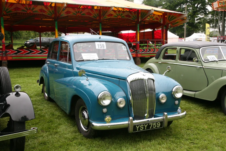 two green antique cars are on display in the grass