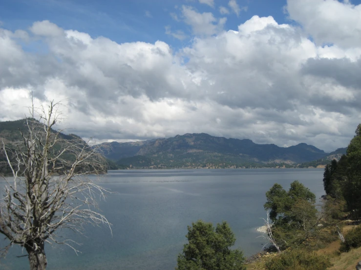 a lake surrounded by mountains with trees and bushes on the side