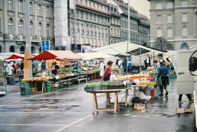 people browsing outside of a farmers market in the rain