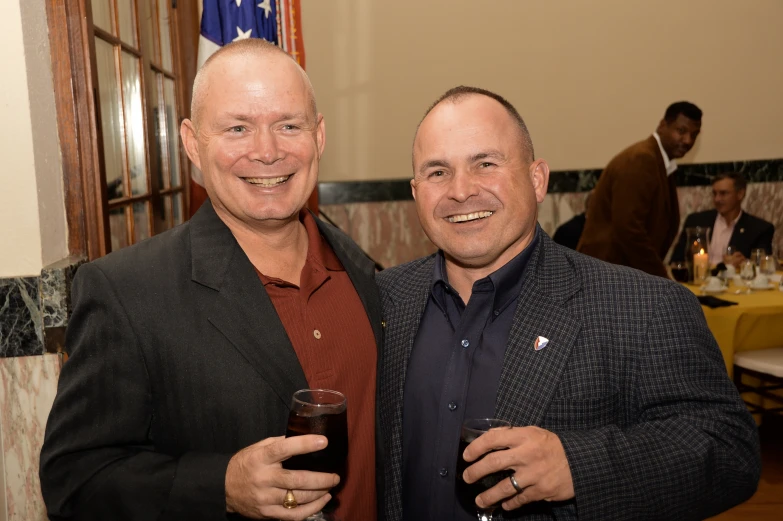 two men standing next to each other holding glasses