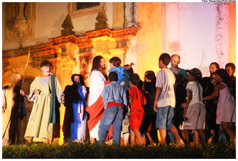 several children standing near a building with a crowd of people