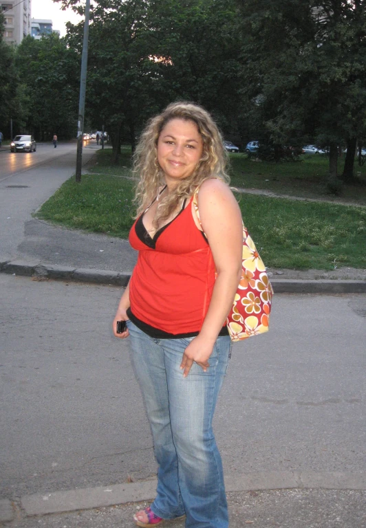 a woman with blond hair and a red shirt stands on the street