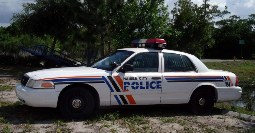 an automobile with a police badge and its lights on is parked next to some water